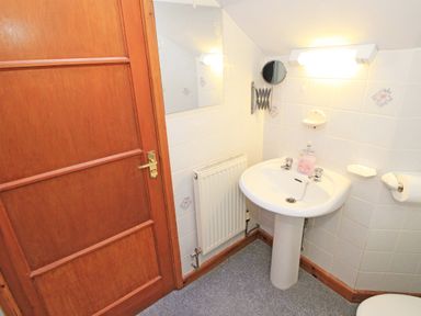 A small bathroom with a wooden door a pedestal sink with soap dispenser a wall-mounted mirror radiator and tiled walls at Artists Cottage in Minffordd near Penrhyndeudraeth