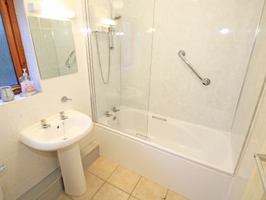 A bathroom with a sink a mirror a bathtub with a shower and a grab bar at Artists Cottage in Minffordd near Penrhyndeudraeth