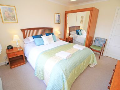 A bedroom with a bed with pillows and folded towels bedside tables with lamps a wooden chair and a wardrobe with mirrored doors at Artists Cottage in Minffordd near Penrhyndeudraeth