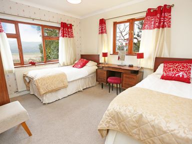 A bedroom with two single beds a wooden desk with a mirror and two red lamps and windows with red and white curtains at Artist's Cottage in Minffordd near Penrhyndeudraeth