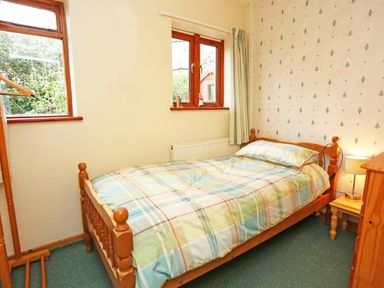 A bedroom with a single wooden bed a bedside table with lamp two windows and a wooden clothes rack at Artists Cottage in Minffordd near Penrhyndeudraeth