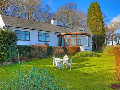 A garden with a white table and chairs set in front of a white house with multiple windows at Artists Cottage in Minffordd near Penrhyndeudraeth