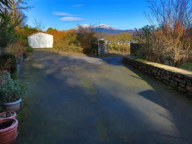 A driveway with a white garage and gate with mountains and houses in the background at Artists Cottage in Minffordd near Penrhyndeudraeth