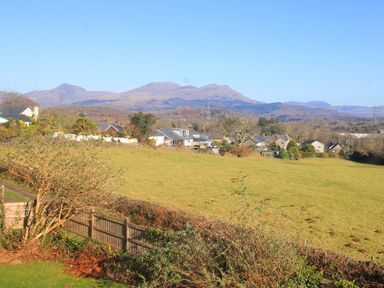 A field with houses in the distance and mountains in the background at Artists Cottage in Minffordd near Penrhyndeudraeth
