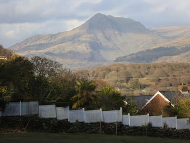 A mountain landscape with trees and houses with white fences in the foreground at Artists Cottage Minffordd near Penrhyndeudraeth
