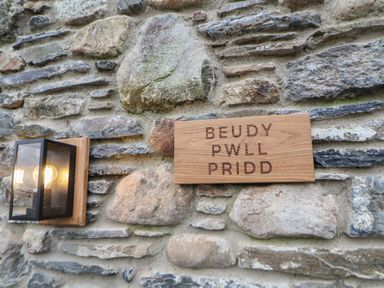 A stone wall with a wooden sign reading Beudy Pwll Pridd and a lit wall-mounted lantern at Beudy Pwll Pridd in Llangollen