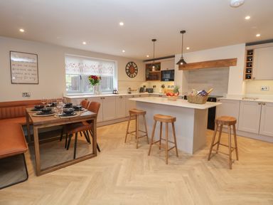 A kitchen with an island and stools next to a dining table with chairs and bench seating at Beudy Pwll Pridd in Llangollen