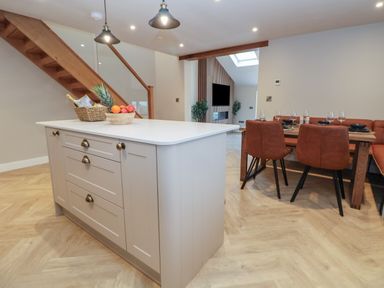 A kitchen island with fruit baskets and a dining table with brown chairs in a kitchen and dining area at Beudy Pwll Pridd in Llangollen