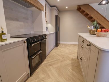 A kitchen with a black oven, white cabinets, a wooden staircase, and fruit bowls on a countertop at Beudy Pwll Pridd in Llangollen