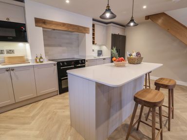 A kitchen with an island and wooden stools a stove microwave and fridge at Beudy Pwll Pridd in Llangollen