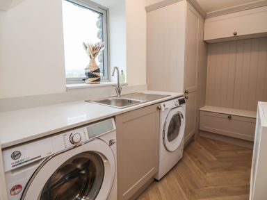 A laundry room with a washing machine dryer sink window and built in cabinets at Beudy Pwll Pridd in Llangollen