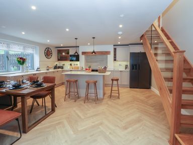 A kitchen and dining area with a wooden dining table set and kitchen island with stools at Beudy Pwll Pridd in Llangollen