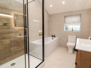 A bathroom with a shower enclosure bathtub toilet sink and a window at Beudy Pwll Pridd in Llangollen