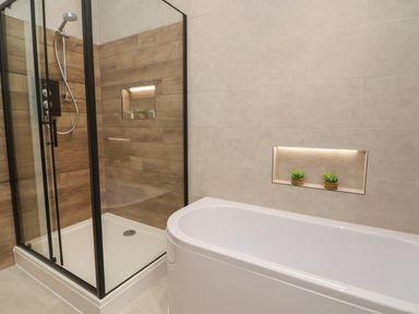 A bathroom with a glass shower enclosure and a white bathtub with small plants in wall niches at Beudy Pwll Pridd in Llangollen