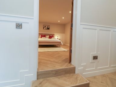 View through doorway into bedroom with bed red cushions and artwork above at Beudy Pwll Pridd in Llangollen