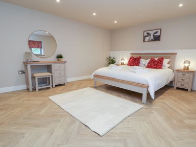 A bedroom with a bed red pillows a rug and a dressing table with a circular mirror at Beudy Pwll Pridd in Llangollen