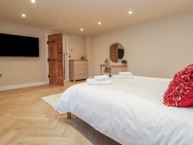 A bedroom with a bed pillows towels a chest of drawers a dressing table with a round mirror and a wall mounted television at Beudy Pwll Pridd in Llangollen