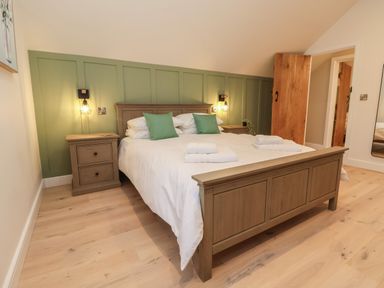 A bedroom with a wooden bed with white bedding and green pillows two wooden nightstands and wall lights at Beudy Pwll Pridd in Llangollen
