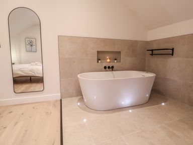 A bathroom with a freestanding bathtub a wall niche with candles and plants a tall mirror reflecting a bed at Beudy Pwll Pridd in Llangollen