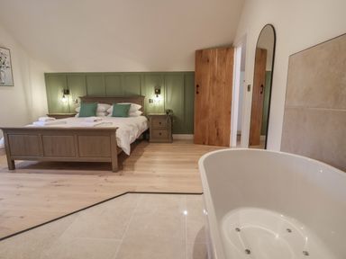 A bedroom with a wooden bed and nightstands next to a bathtub at Beudy Pwll Pridd in Llangollen