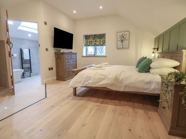 A bedroom with a bed pillows a dresser and a wall-mounted TV near a bathroom with tiled walls at Beudy Pwll Pridd in Llangollen
