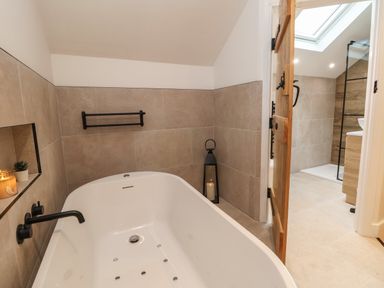 A bathroom with a bathtub a wooden door and a shower area at Beudy Pwll Pridd in Llangollen