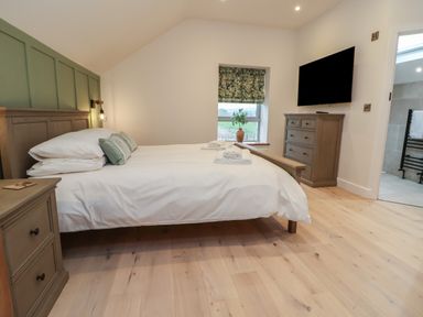 A bedroom with a wooden bed white bedding a wooden chest of drawers a window and a wall-mounted TV at Beudy Pwll Pridd in Llangollen
