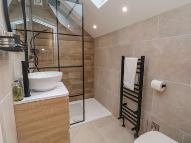 A bathroom with a wooden cabinet and white sink a black towel rack with a towel and a glass shower enclosure at Beudy Pwll Pridd in Llangollen