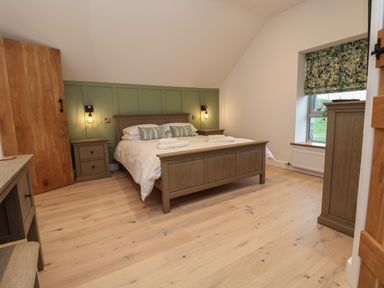 A bedroom with a bed between two bedside tables and a window with a floral blind at Beudy Pwll Pridd in Llangollen