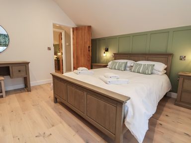 A bedroom with a wooden bed and side tables with white linens and green pillows at Beudy Pwll Pridd in Llangollen