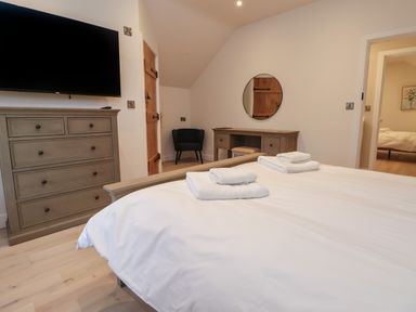 A bedroom with a bed, folded towels, a chest of drawers, a wall-mounted TV, a dressing table with a round mirror, and a chair at Beudy Pwll Pridd in Llangollen