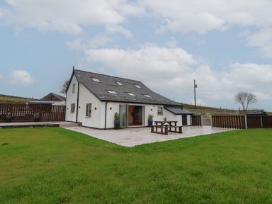 A house with a tiled patio and wooden picnic table in a grassy yard at Beudy Pwll Pridd in Llangollen