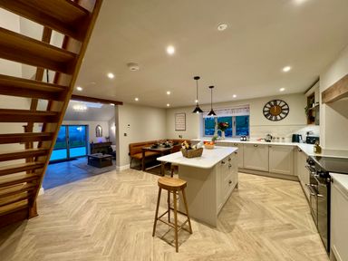 A kitchen with an island and a wooden stool near a dining nook and open living area at Beudy Pwll Pridd in Llangollen