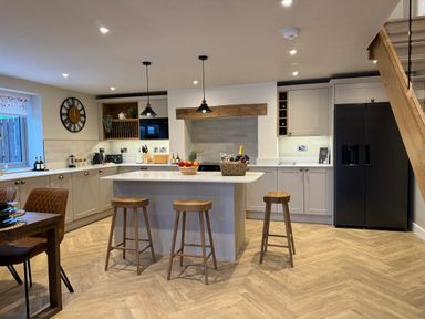 A kitchen with island and three wooden stools a black refrigerator and dining table with chairs at Beudy Pwll Pridd in Llangollen