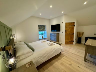 A bedroom with a double bed a wooden door a window with a plant a wall-mounted television and wooden furniture at Beudy Pwll Pridd in Llangollen