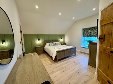 A bedroom with a wooden bed with white bedding two bedside tables a dresser a round mirror and a window with floral Roman blind at Beudy Pwll Pridd in Llangollen