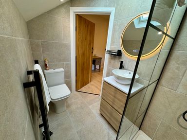 A bathroom with a toilet a sink with vanity and a round mirror with lights at Beudy Pwll Pridd in Llangollen