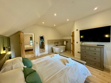 A bedroom with a bed, towels, a wall-mounted television, a chest of drawers, a bathtub, and a mirror at Beudy Pwll Pridd in Llangollen
