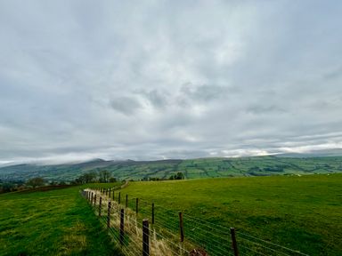 A rural landscape with green fields divided by a wire fence and hills in the background at Beudy Pwll Pridd in Llangollen