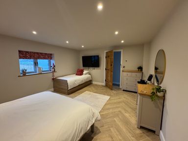 A bedroom with two beds a dresser a round mirror a television on the wall and a wooden door at Beudy Pwll Pridd in Llangollen