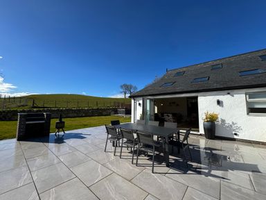 An outdoor patio with a dining table and chairs next to a white building with skylights at Beudy Pwll Pridd in Llangollen