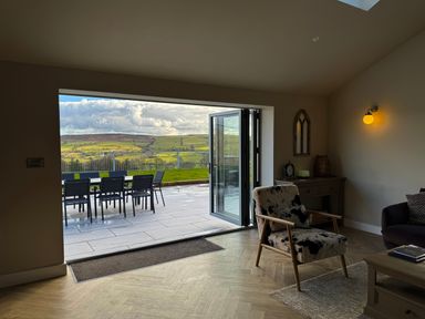 A living room with a patterned armchair a desk lamp and an outdoor dining table on a tiled patio at Beudy Pwll Pridd in Llangollen