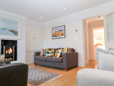 A living room with a gray sofa with patterned cushions a fireplace and a framed picture above the sofa at 6 Willows Green in Aldeburgh