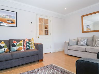 A living room with two sofas with cushions a wall mirror a glass door and a framed picture at 6 Willows Green in Aldeburgh