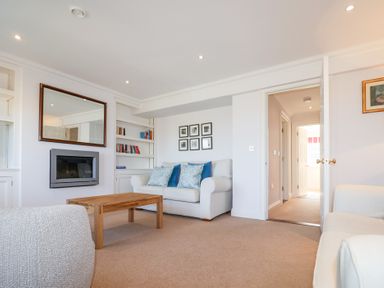 A living room with a wooden coffee table two white sofas wall-mounted fireplace bookshelves and framed pictures at 6 Willows Green in Aldeburgh