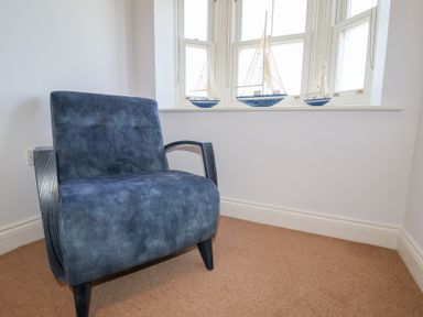 A blue armchair next to a window with three model sailboats on the windowsill at 6 Willows Green in Aldeburgh