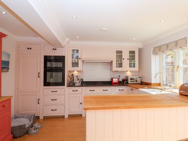 A kitchen with white cabinets wooden countertops a double oven a red toaster a microwave and a dog bed with food and water bowls at 6 Willows Green Aldeburgh