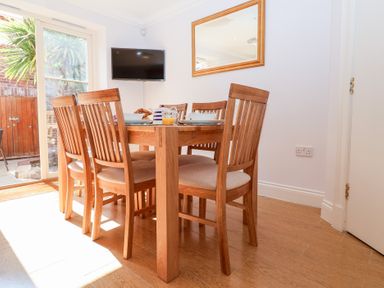 A dining area with wooden chairs and table near a glass door and a wall-mounted television at 6 Willows Green Aldeburgh