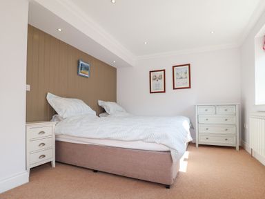 A bedroom with a double bed white bedside table chest of drawers and framed pictures on the walls at 6 Willows Green in Aldeburgh