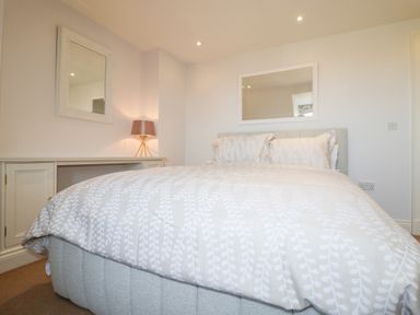 A bedroom with a bed with patterned bedding a lamp on a cabinet and two mirrors on the walls at 6 Willows Green in Aldeburgh